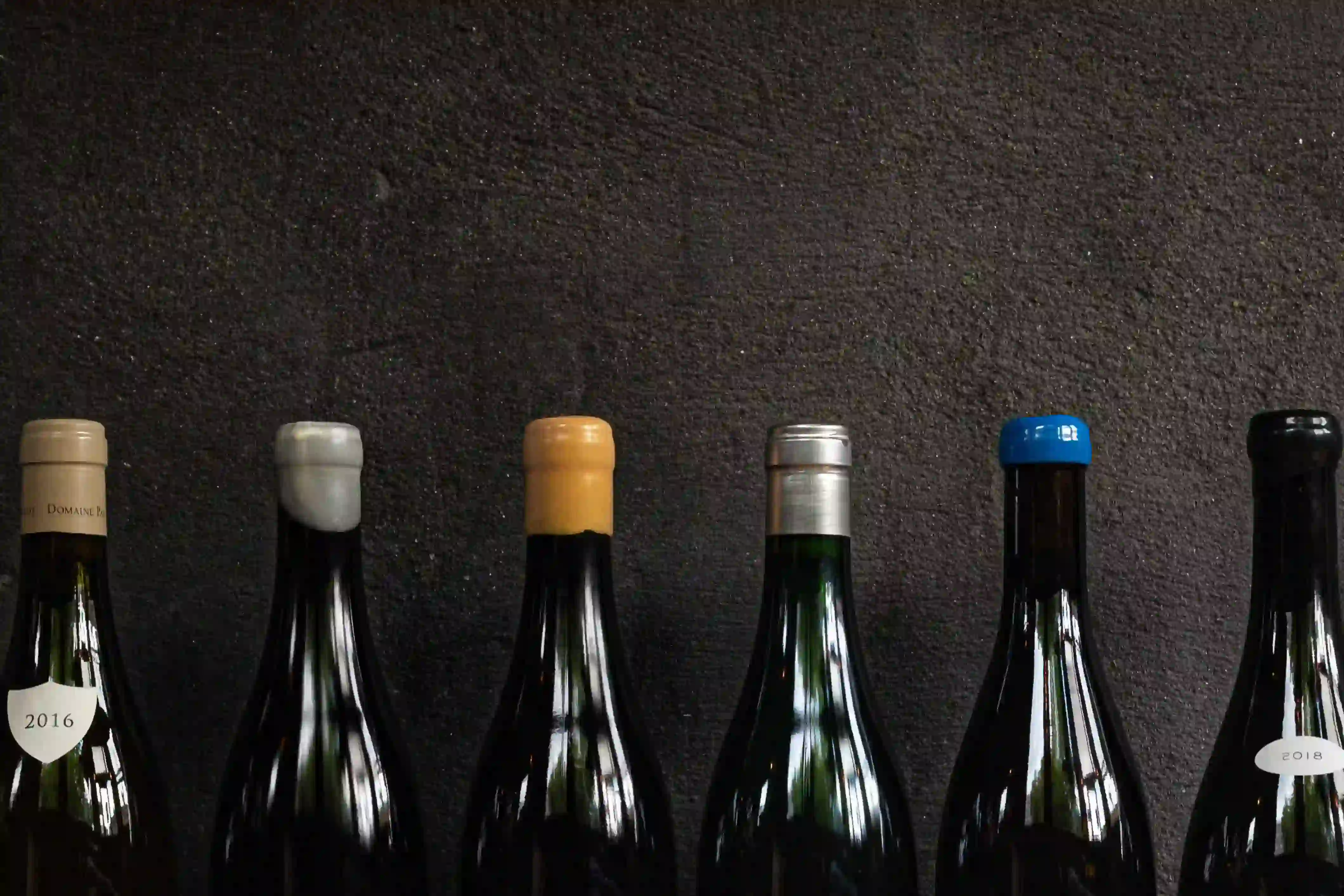 A row of wine bottles against a dark wall, necks and capsules in a line